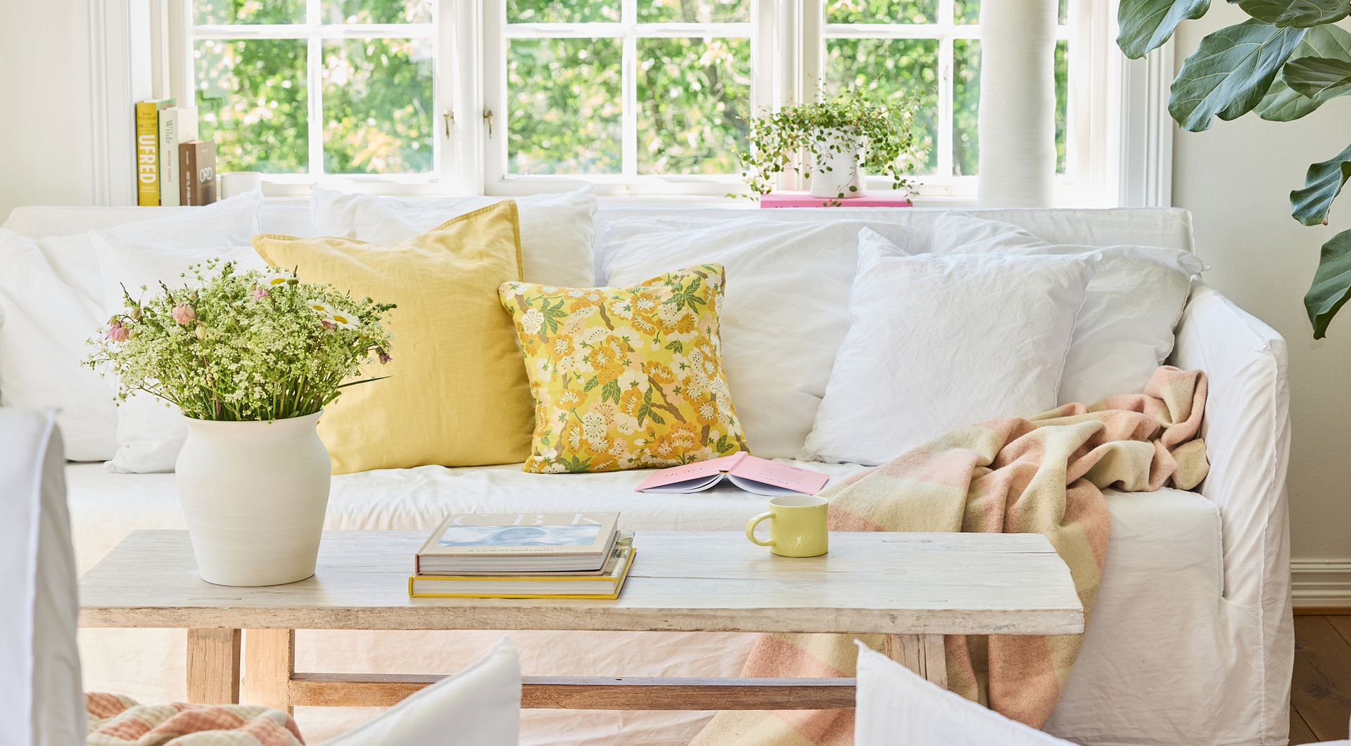 Vase og gul kopp i porselen, som dekor i stue med sofa, puter og blomster