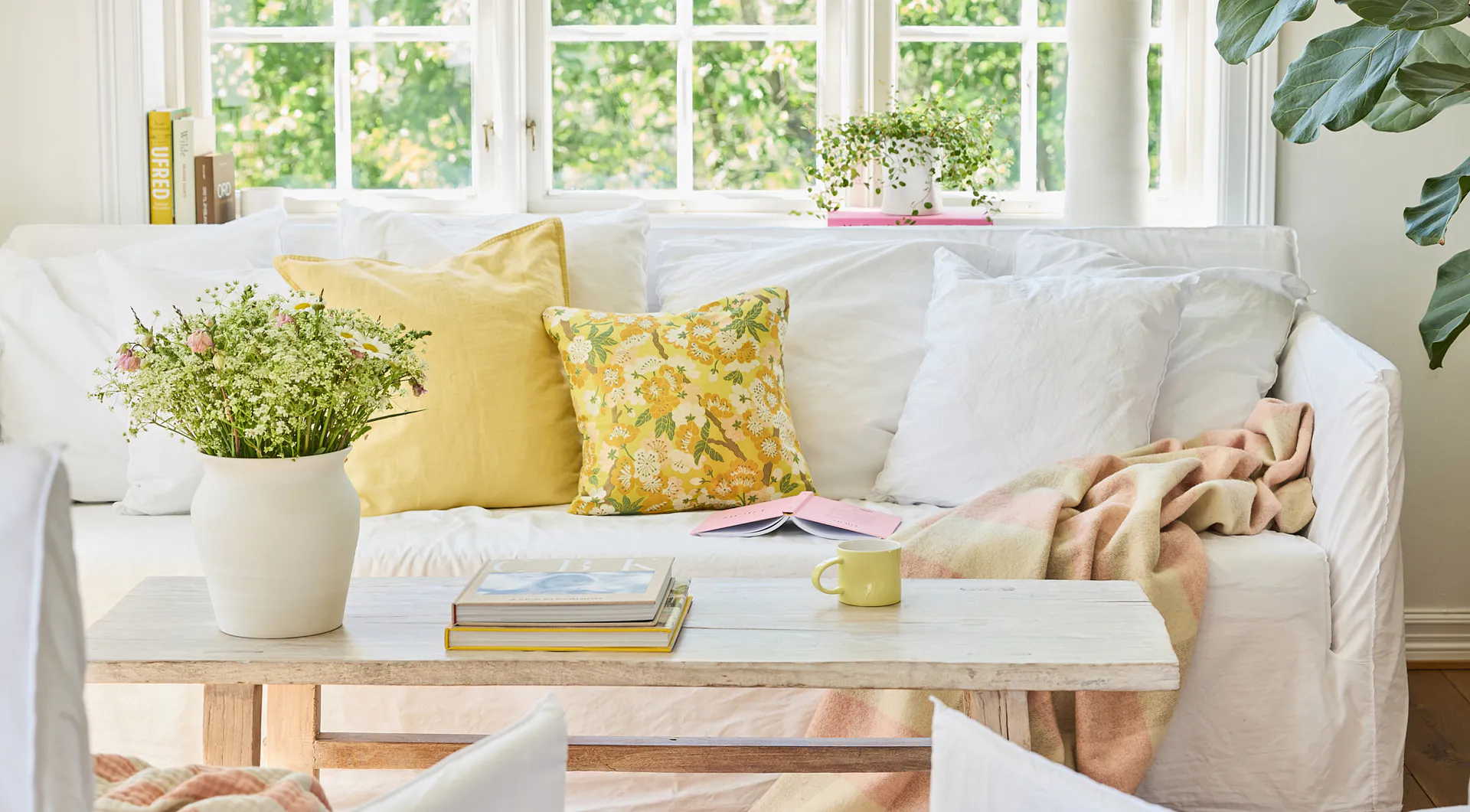 Vase og gul kopp i porselen, som dekor i stue med sofa, puter og blomster